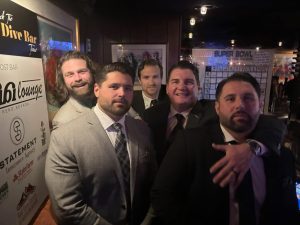 Group of young men wearing suits and smiling for the camera.